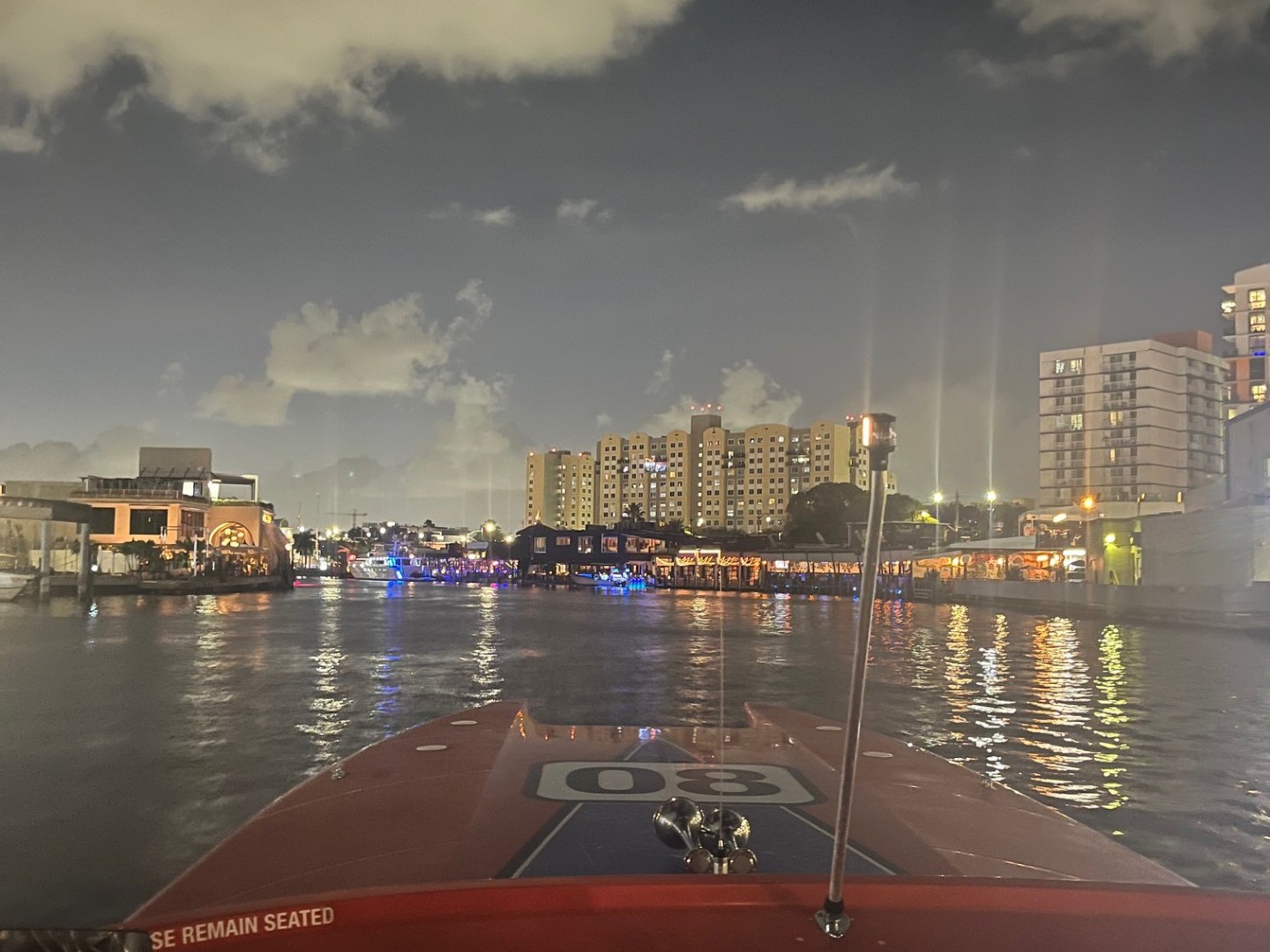 View from a boat at night with city lights and cloudy sky.