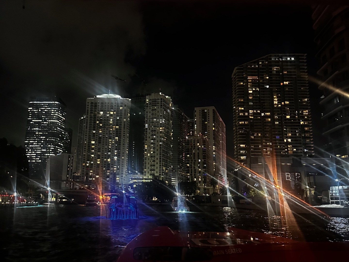 Night city skyline with colorful lights reflecting on water from a boat.