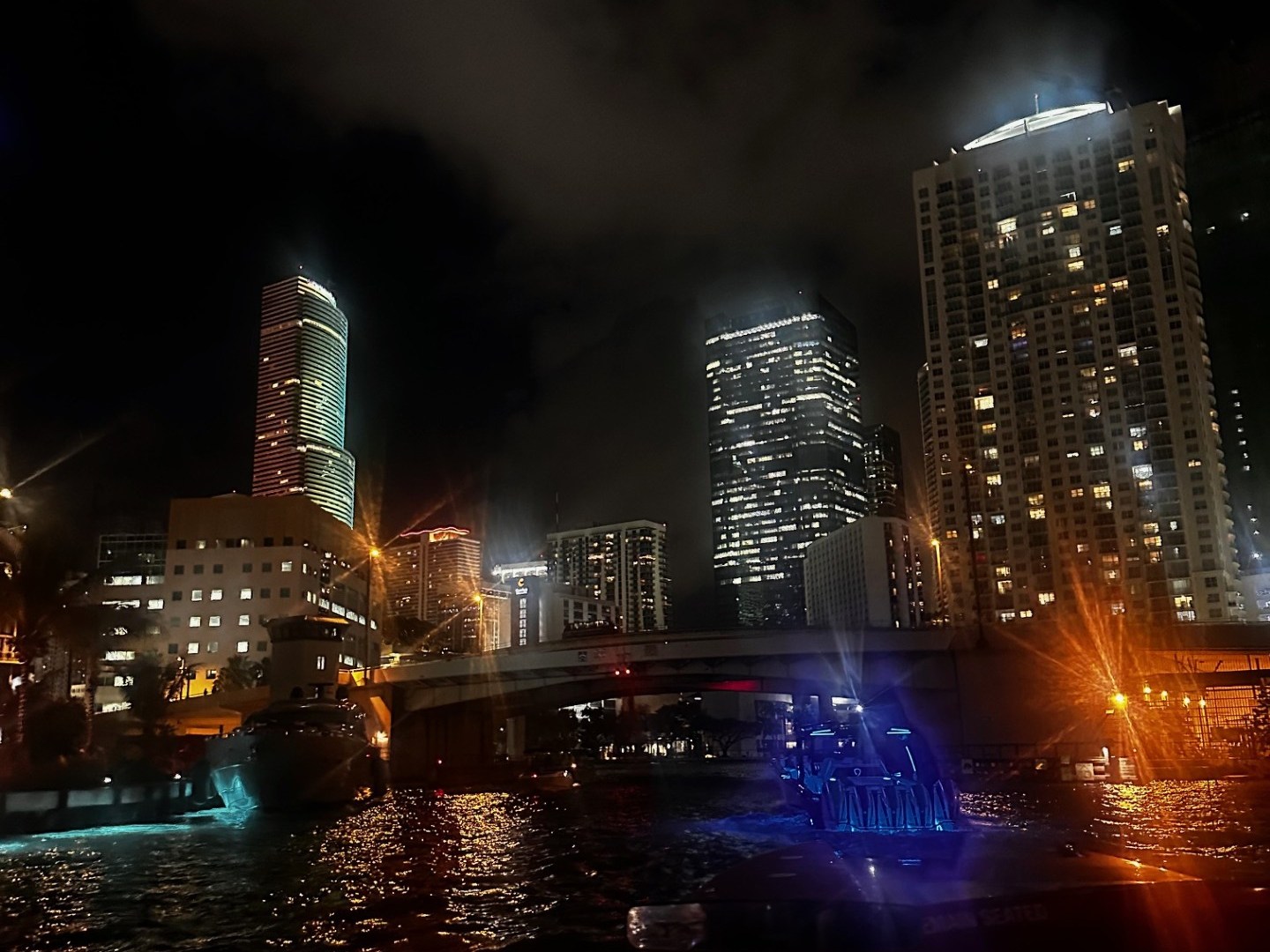 City skyline at night with lit buildings, bridge, and water reflections.