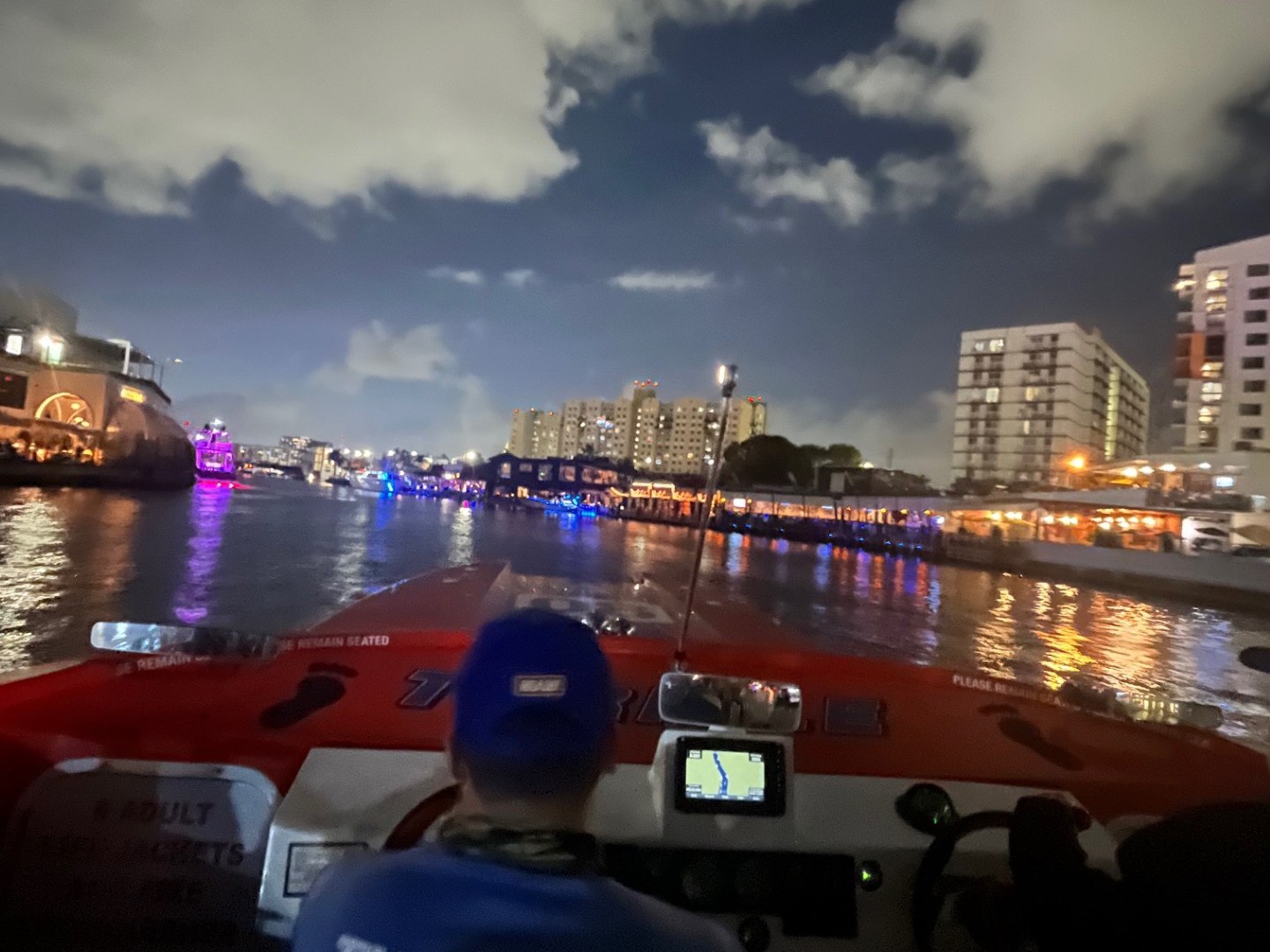Night view from a speedboat with city skyline and clouds.