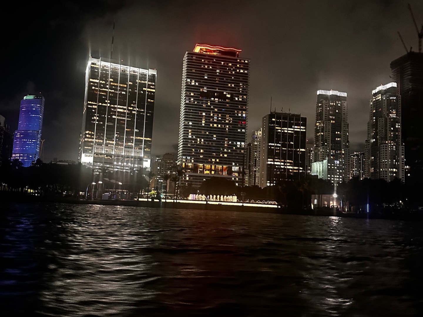 Night cityscape with lit skyscrapers reflecting on dark water.
