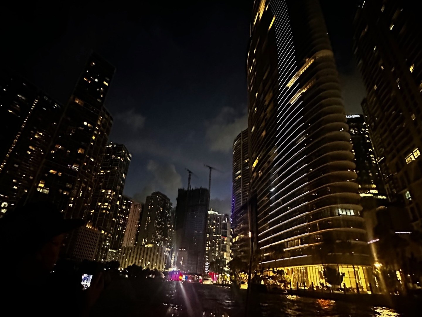 Night cityscape with tall illuminated buildings and a person taking a photo.